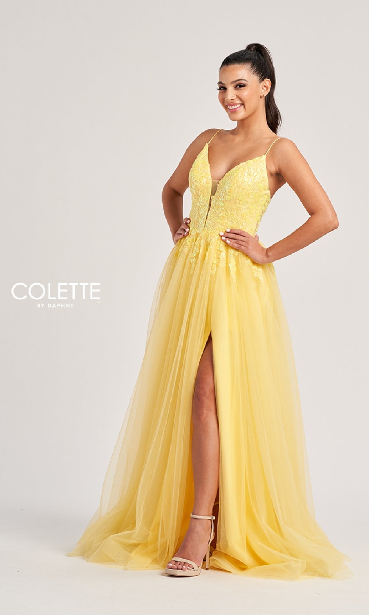 Woman wearing the Colette CL8030, a sleeveless yellow long prom dress with a sequined bodice, deep V-neckline, floral detailing, and a tulle A-line skirt featuring a thigh-high front slit, posing against a plain background.